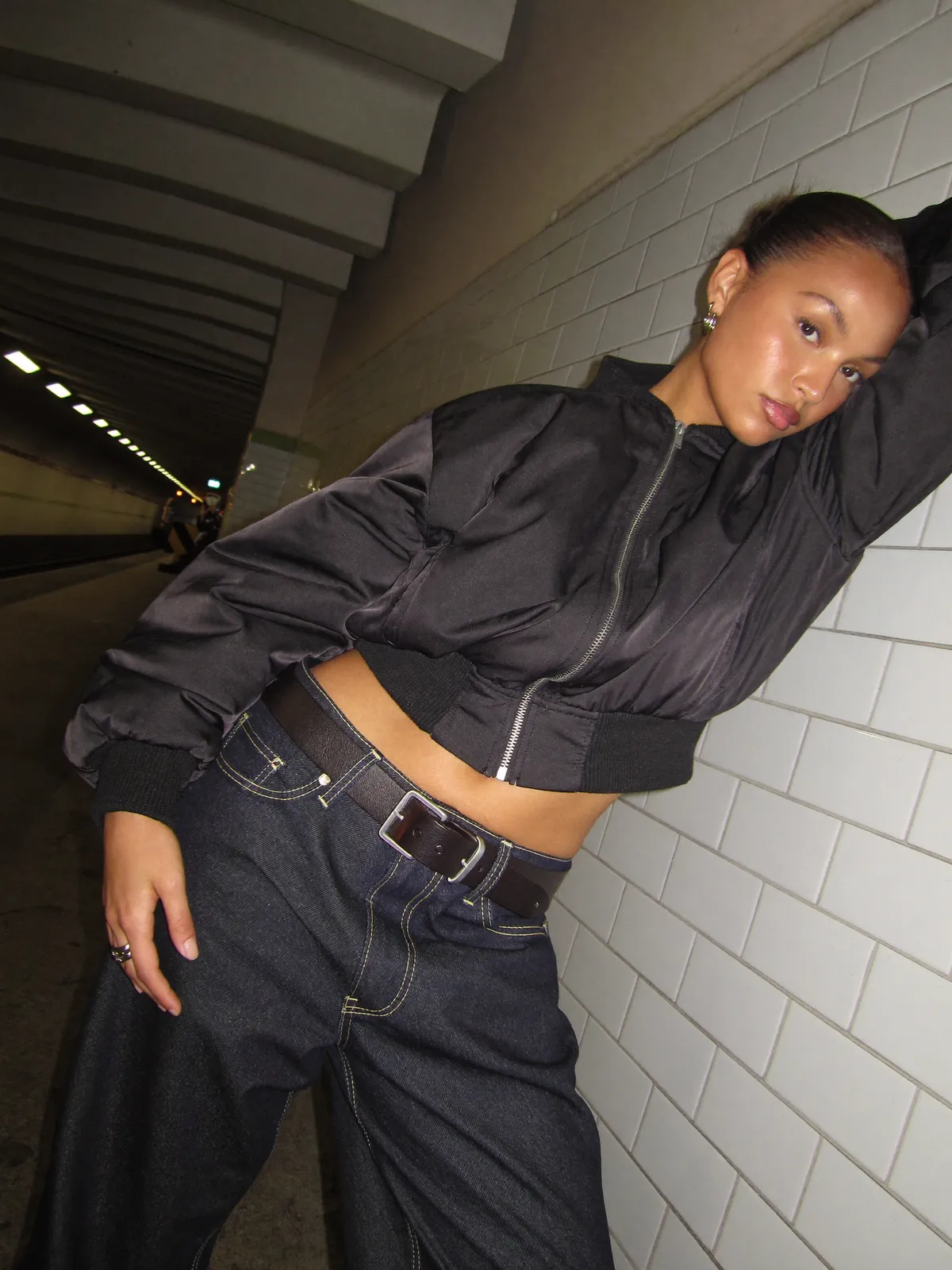 AI fashion shoot: a woman in a cropped black bomber jacket and dark denim against the white tiles of a subway tunnel